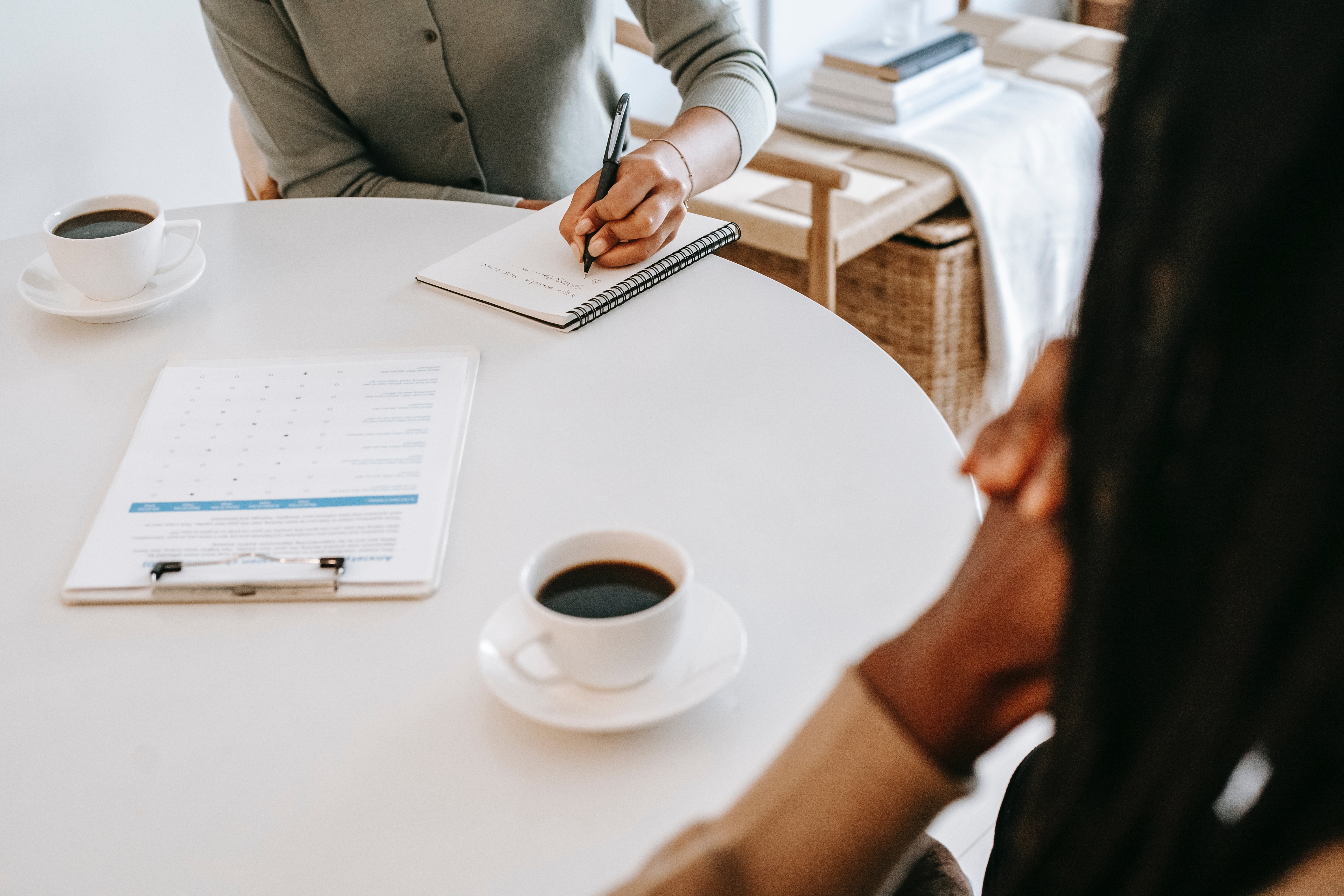 Close-up of a table with two coffee cups, a clipboard, and two people sitting across of each other