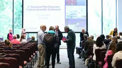 Photo of a display of slides that read "3rd APDP conference, June 2025" in the background. There are people sitting and standing in a group in the foreground.