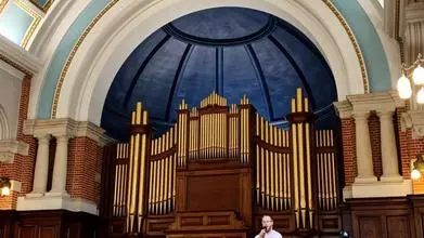 The photo shows six people sat on chairs and one standing, speaking in a microphone, on a stage in the University of Reading's Great Hall