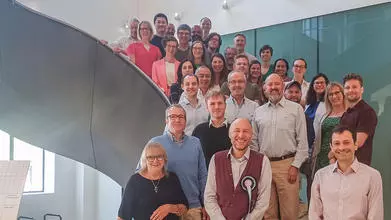 Group photo of the PAINSTORM consortium. About 25 people are standing on a large spiral staircase.
