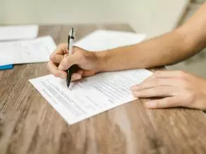 A close-up on the hand and forearm of a person filling in a paper questionnaire